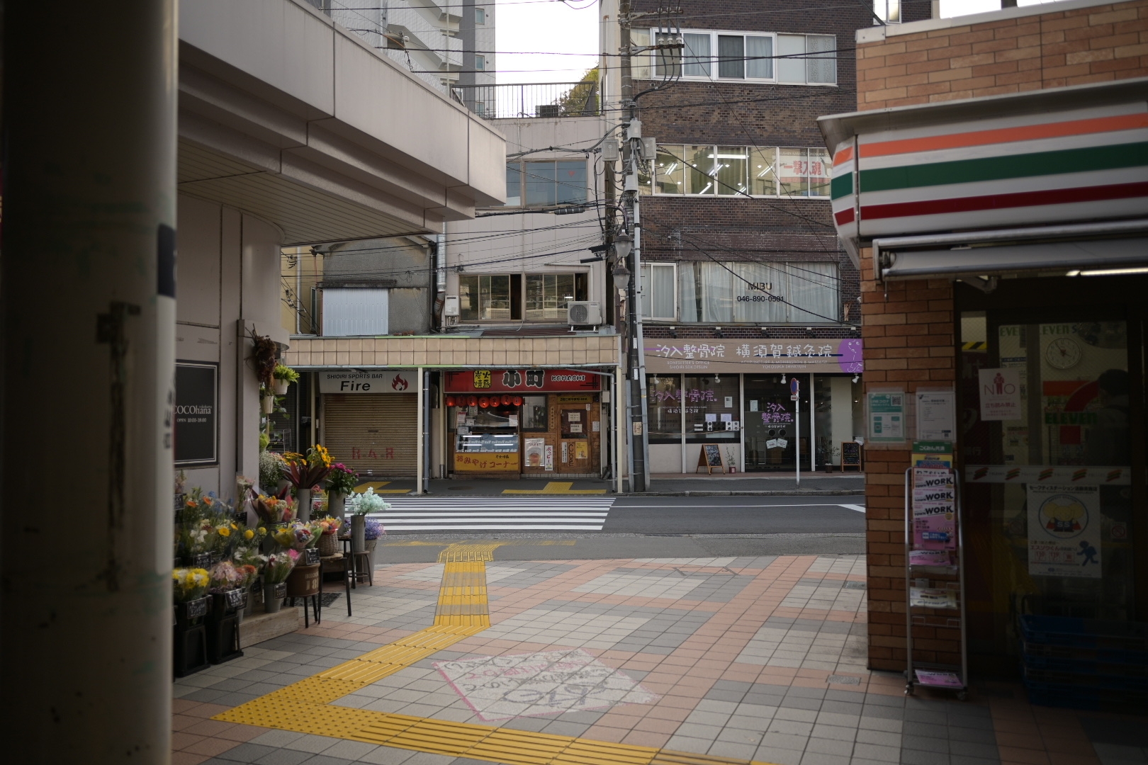 A quiet street scene in Yokosuka, Japan, showing a flower shop and a 7-Eleven, reflecting the author's connection to the city.